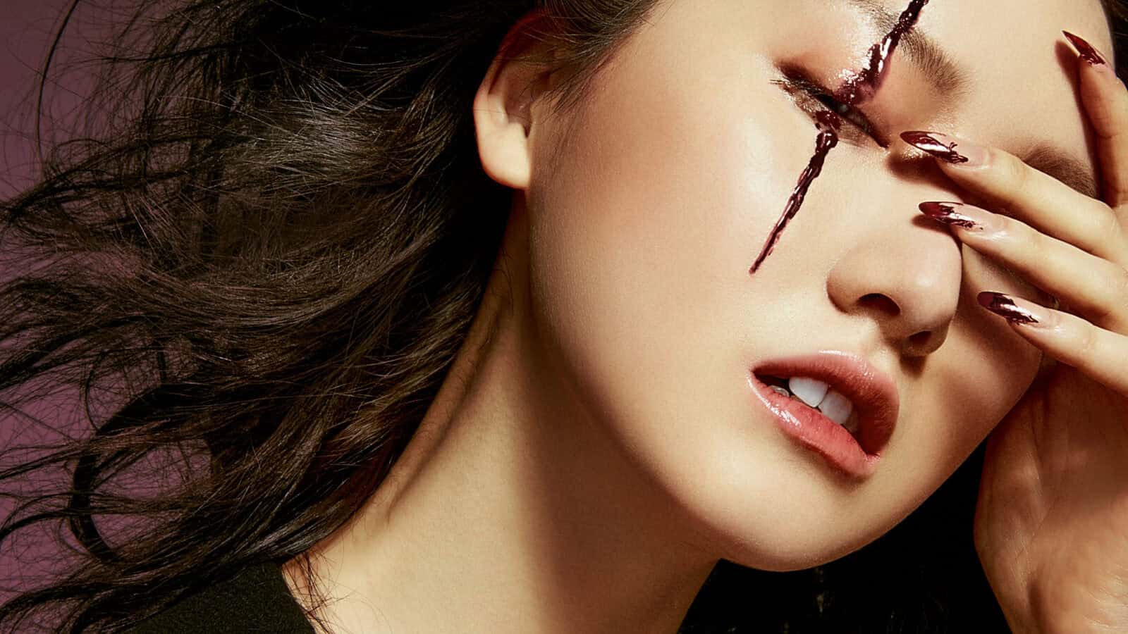 A woman with dramatic makeup and a painted face, featuring a cross design over her eye.